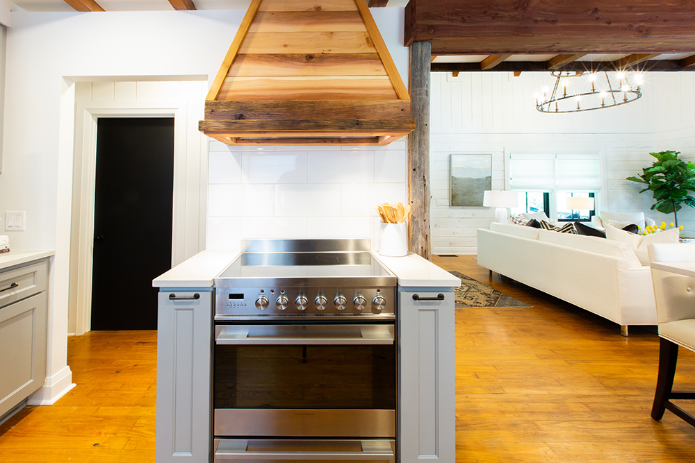 Warm welcoming kitchen with a large high end over topped with an oven hood that’s covered in salvaged rough finished wood.