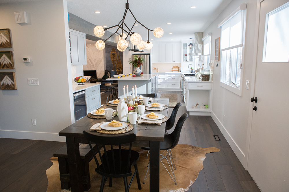 Bright and modern dining room featured on The Property Brothers on HGTV with a long dark wood table set with white plates and mugs, four dining chairs and a long bench, and an abstract globe chandelier