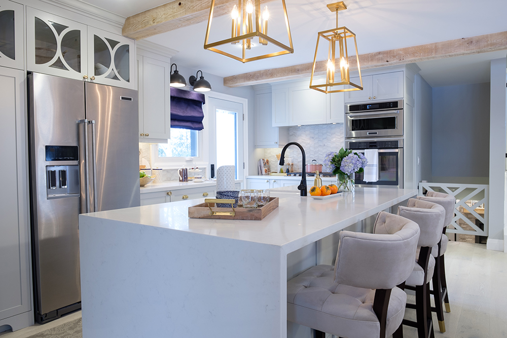 A modern kitchen with a waterfall edged kitchen island and two large gold chandeliers