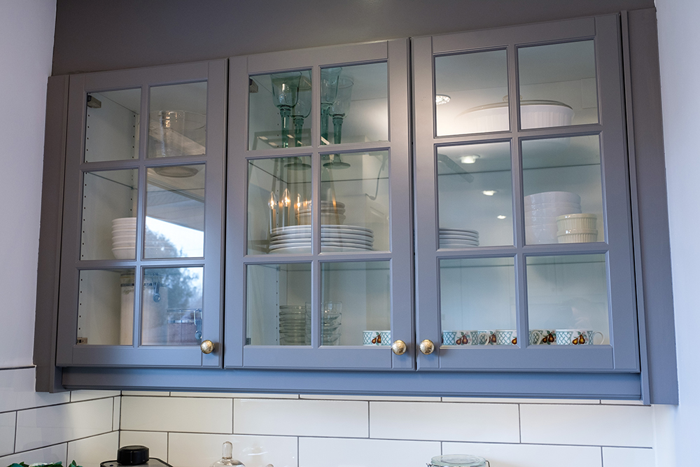 Grey kitchen cabinets with glass doors and white plates and bowls inside