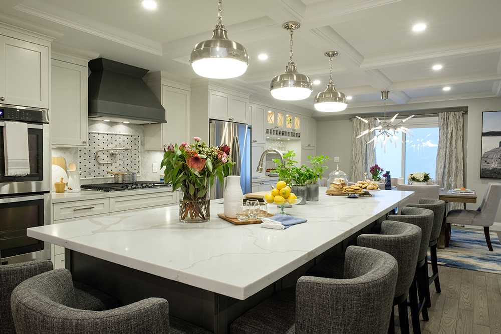 Large white centre island surrounded by plush grey bar stools in a modern kitchen with three pendant lights