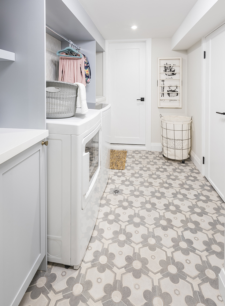 Cute modern laundry room with grey daisy tiled floors, white washer and dryer, and a drying rack with hanging clothes