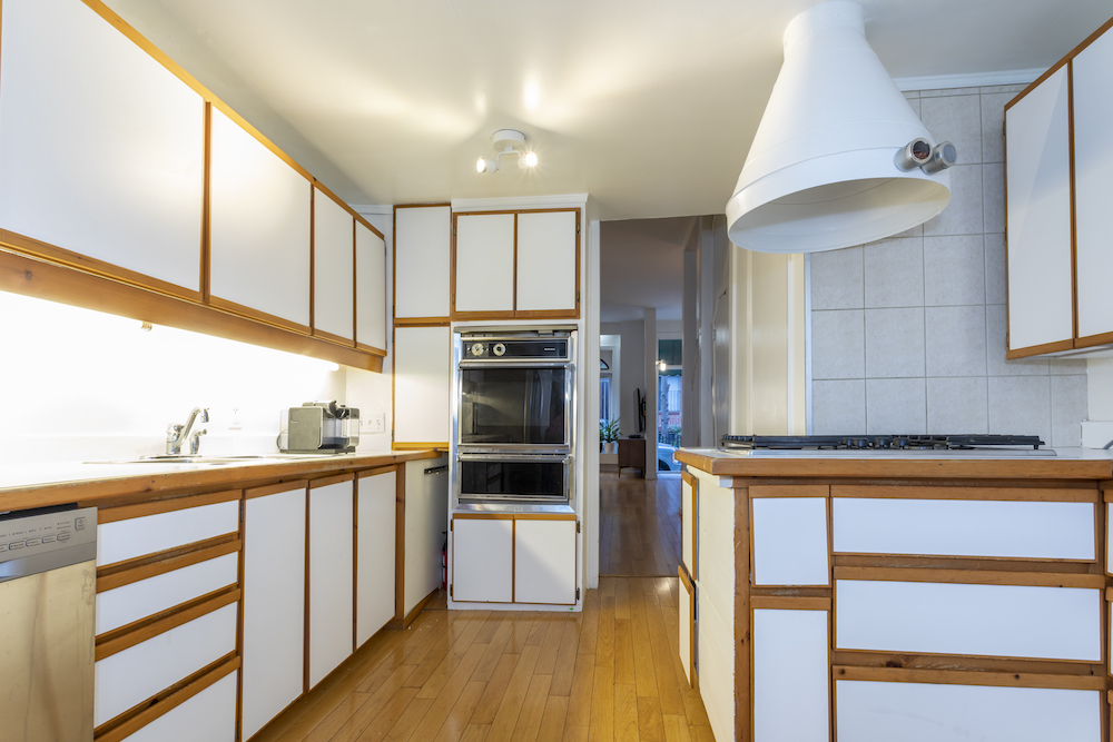 A dated kitchen with white cabinets, old appliances and blonde wood floors