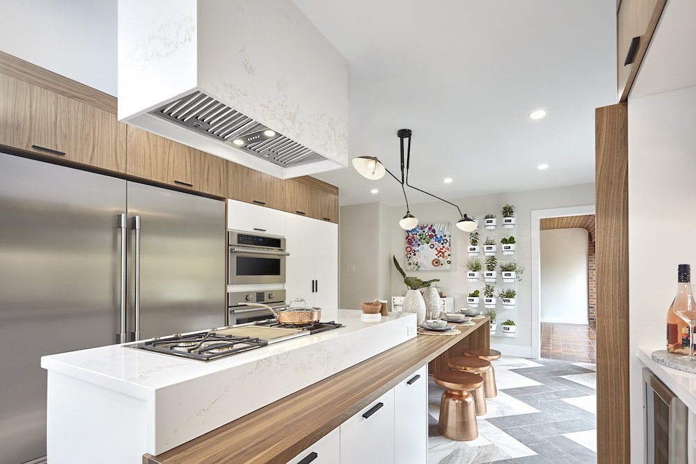 Modern kitchen full of bleached oak cabinets and a large sit at kitchen island with a stovetop and quartz hood