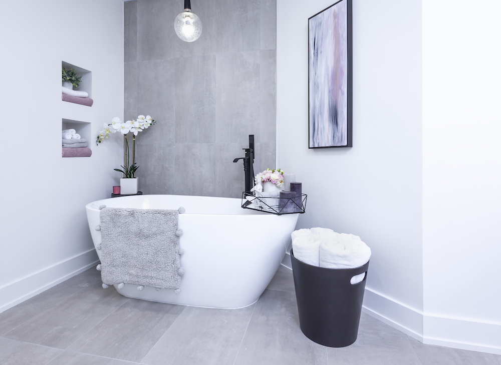 Modern white soaker tub sits in a chic bathroom with grey tile floors and feature wall behind it