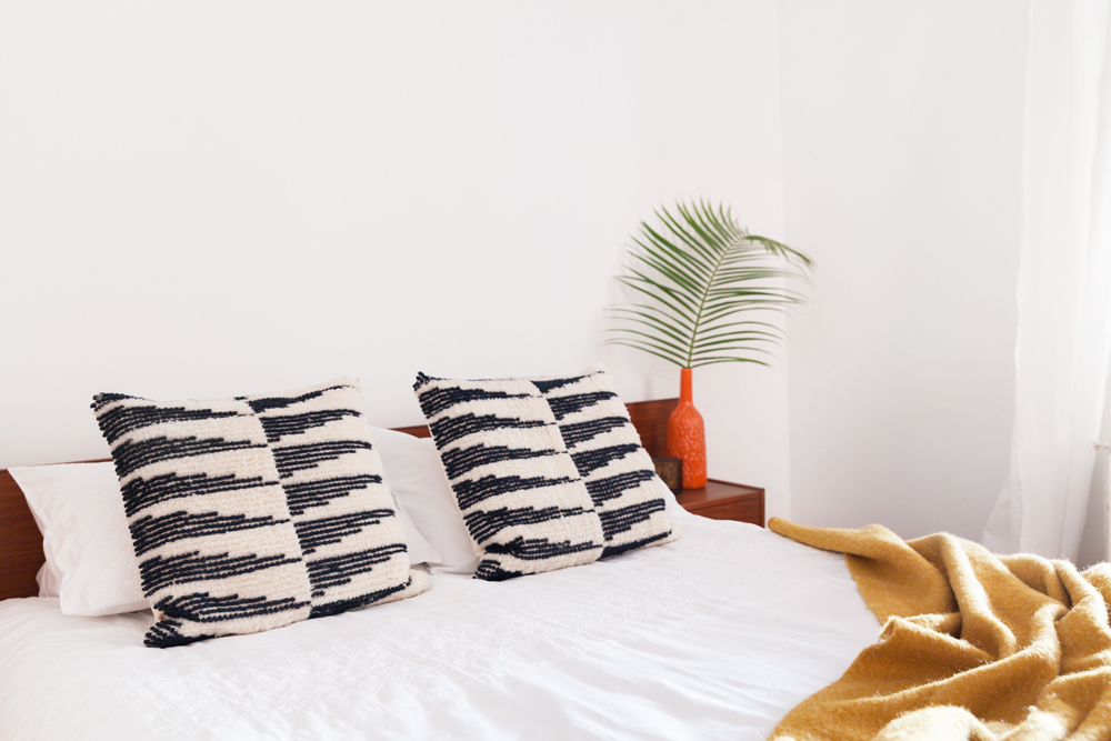 Patterned throw pillows on a guest bed in a room with potted plants