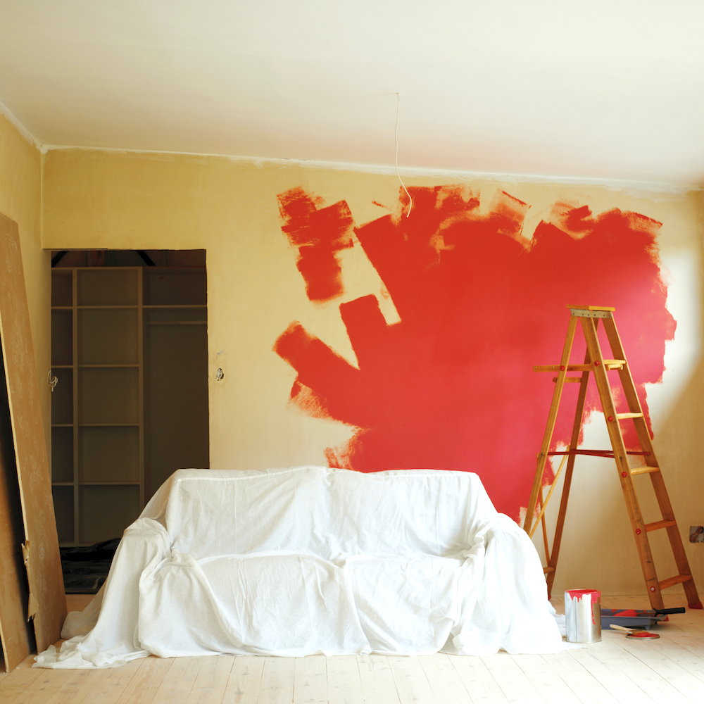 Covered couch with a ladder and wall half painted in red paint