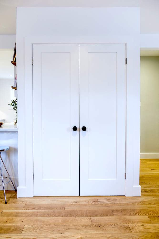 White front hall coat closet with round black handles and a light oak wood floor