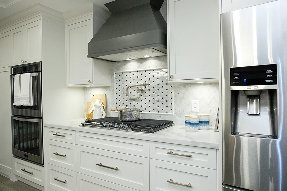 White marble tile backsplash in a modern kitchen with a countertop range and oven hood