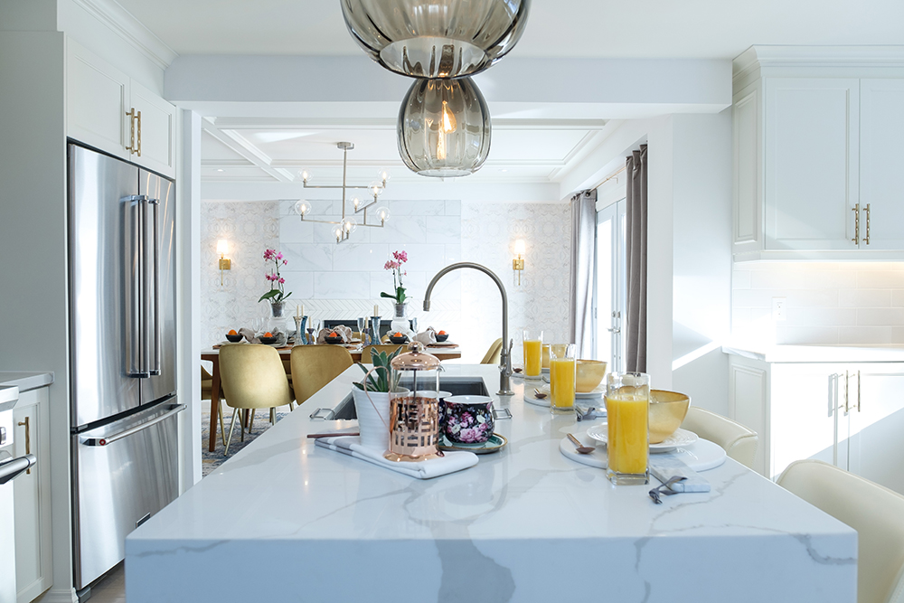 Chic white modern kitchen with white quartz countertop with a water fall edge set with glasses of orange juice