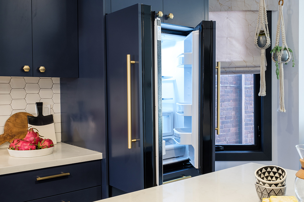 Fridge opens up out of dark blue kitchen cabinetry and white countertops