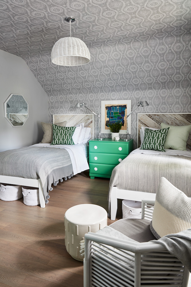 Chic guest bedroom with two twin beds, a green dresser and wallpaper on the wall and ceiling