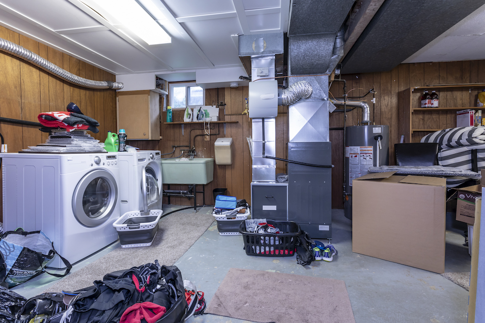 A dirty basement filled with hockey equipment, a washer and dryer set and an expose HVAC system