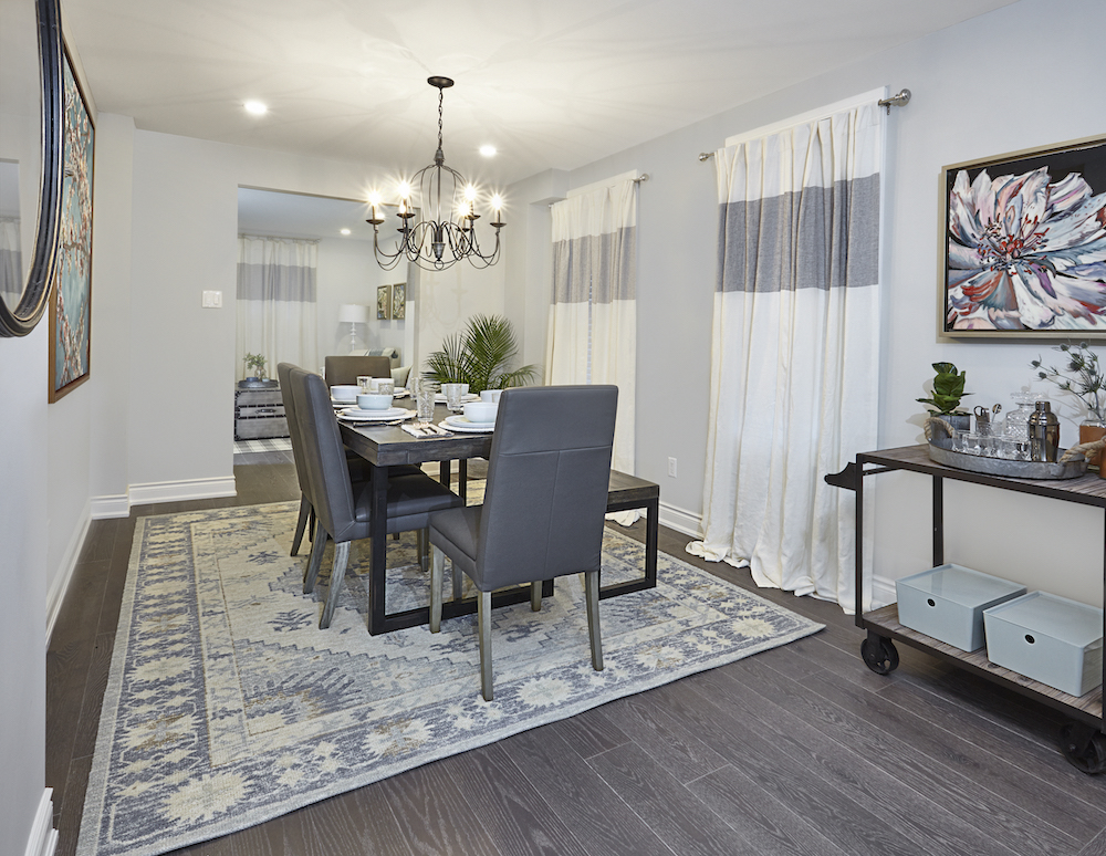 A modern grey dining room with dark grey engineered wood floors, large white and blue rug, and white and grey striped drapes