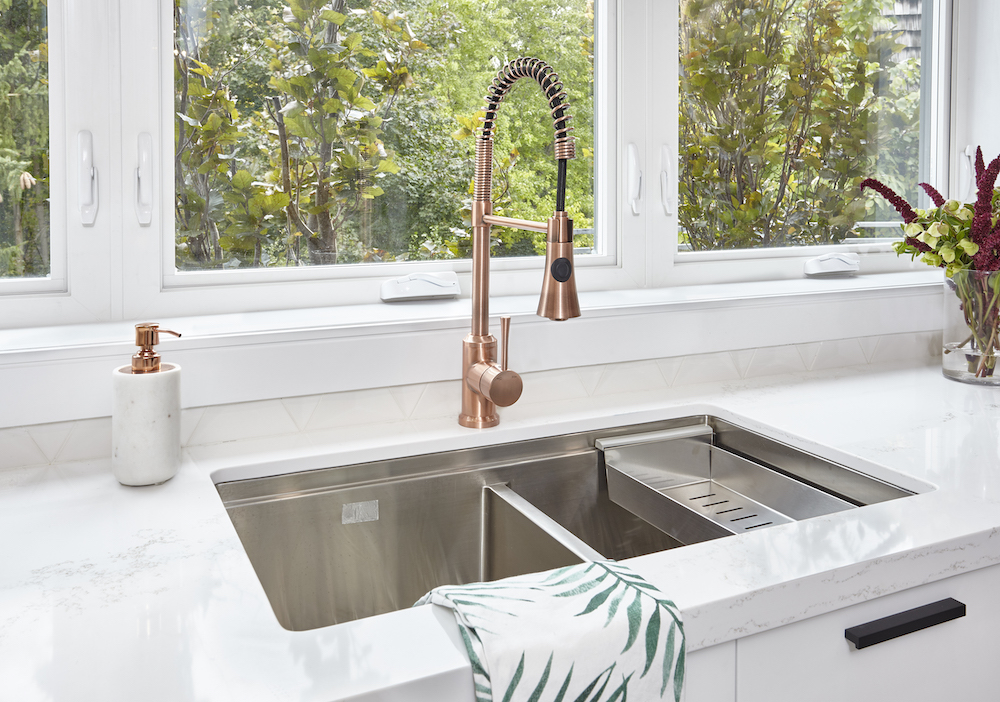 Large stainless steel sink set in a white quartz countertop with a chic bronze faucet