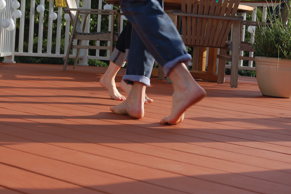Two sets of barefoot dancing feet on a deck featuring BEHR PREMIUM Solid Colour Waterproofing Stain & Sealer in Redwood Naturaltone