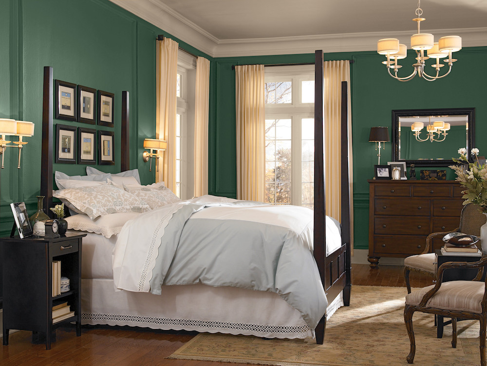 Opulent bedroom with a dark four poster bed, wooden dresser, tall white drapes and walls painted in BEHR’s Vine Leaf N400-7