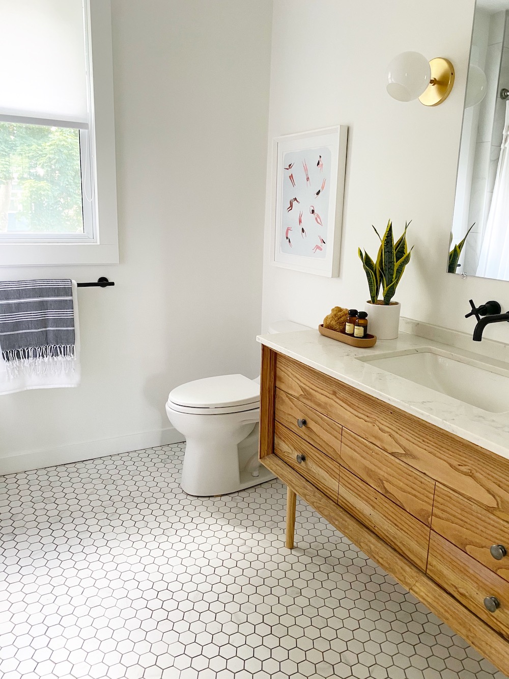 Beautiful white bathroom designed and styled by The Property Stylist Inc. with a wooden vanity, undermounted sink, black hardware, white hexagon tile floors, and a white toilet