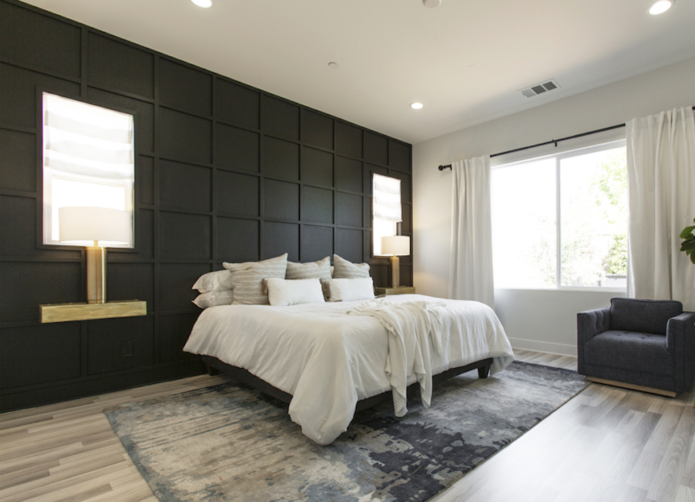 Chic bedroom with blonde hardwood, a large patterned area run, and a black panelled accent wall with built-in lamps and windows as featured on Boise Boys for HGTV Canada