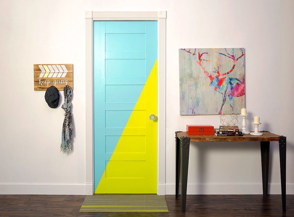 In a white hallway with a hall table and elk artwork on the wall, there is also a blue and yellow bedroom door that’s painted on the diagonal with BEHR Anime P340-5 and Rainwater P450-3