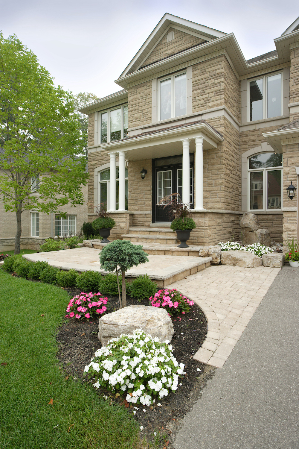 Classic two story stone house with four white columns on the front porch, a black double front door, a landscaped front yard, and a stone paver front path and entryway steps