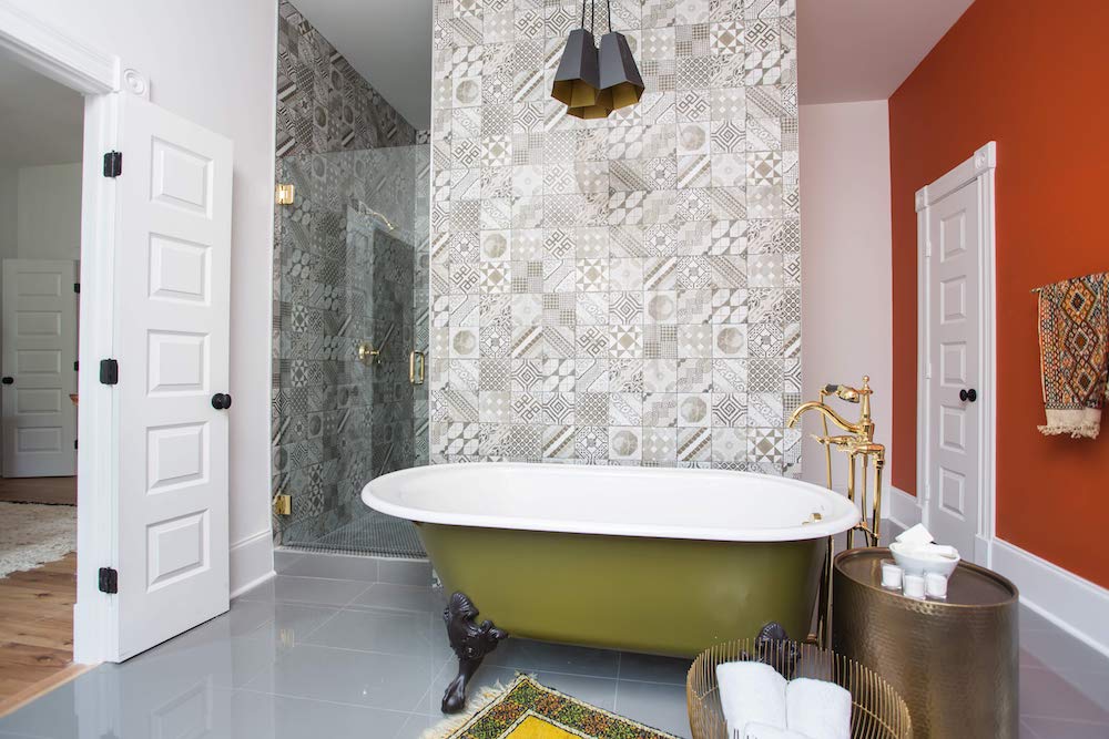 Masters of Flip bohemian Victorian house master suite ensuite bathroom with green clawfoot bathtub, geometric patterned wall tile and bright orange wall