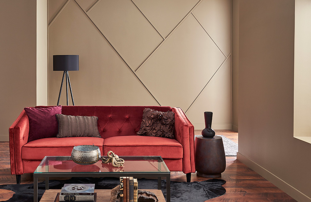 Modern living room with a red velvet couch, glass topped coffee table, black floor lamp, and walls painted in BEHR Pure Earth PPU7-05