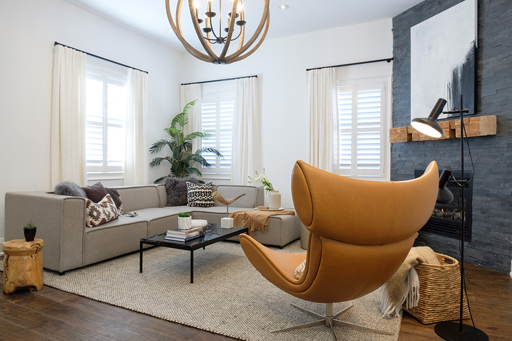 Chic, white Southwestern inspired living room with matte black curtain rods hung with soft white drapes, a black coffee table, a black floor lamp, large grey sectional couch, tan leather egg chair, and a large gold globe chandelier
