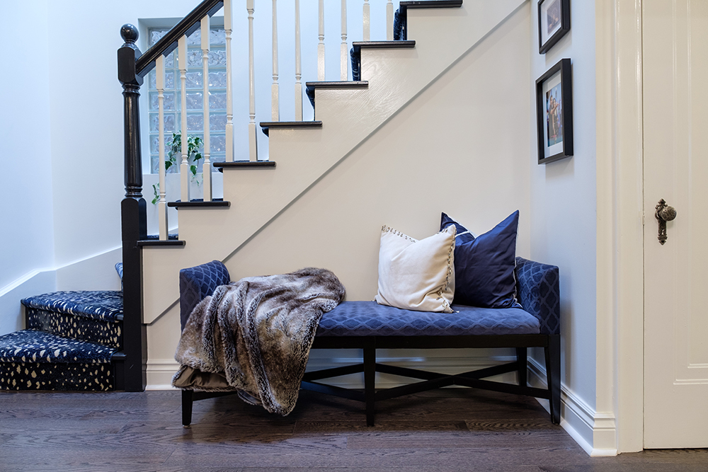 A blue velvet bench sits in front of a black and white painted bannister leading up to the second floor