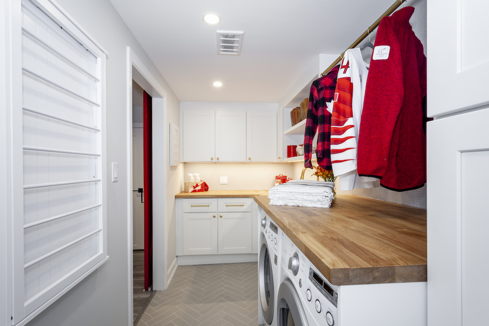New basement laundry room with herringbone tile floors, a butcherblock counter, white cabinets and a two drying racks