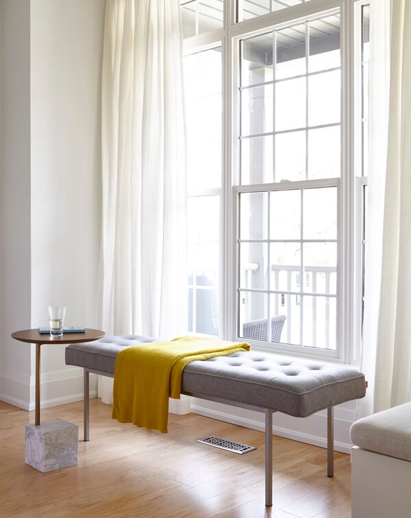 grey tufted bench with mustard throw in front of paned window with white drapes