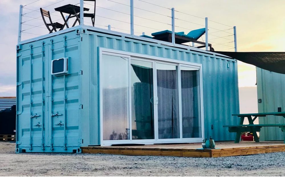 Blue shipping container with glass sliding doors and a deck on the roof