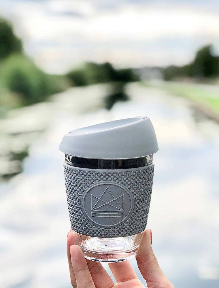 hand holding glass and grey reusable coffee cup