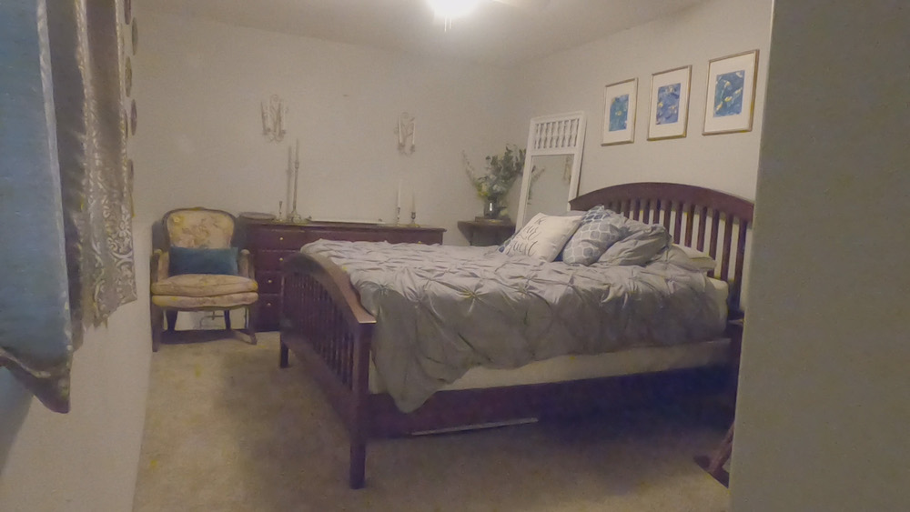 dimly lit guest bedroom before with grey bed