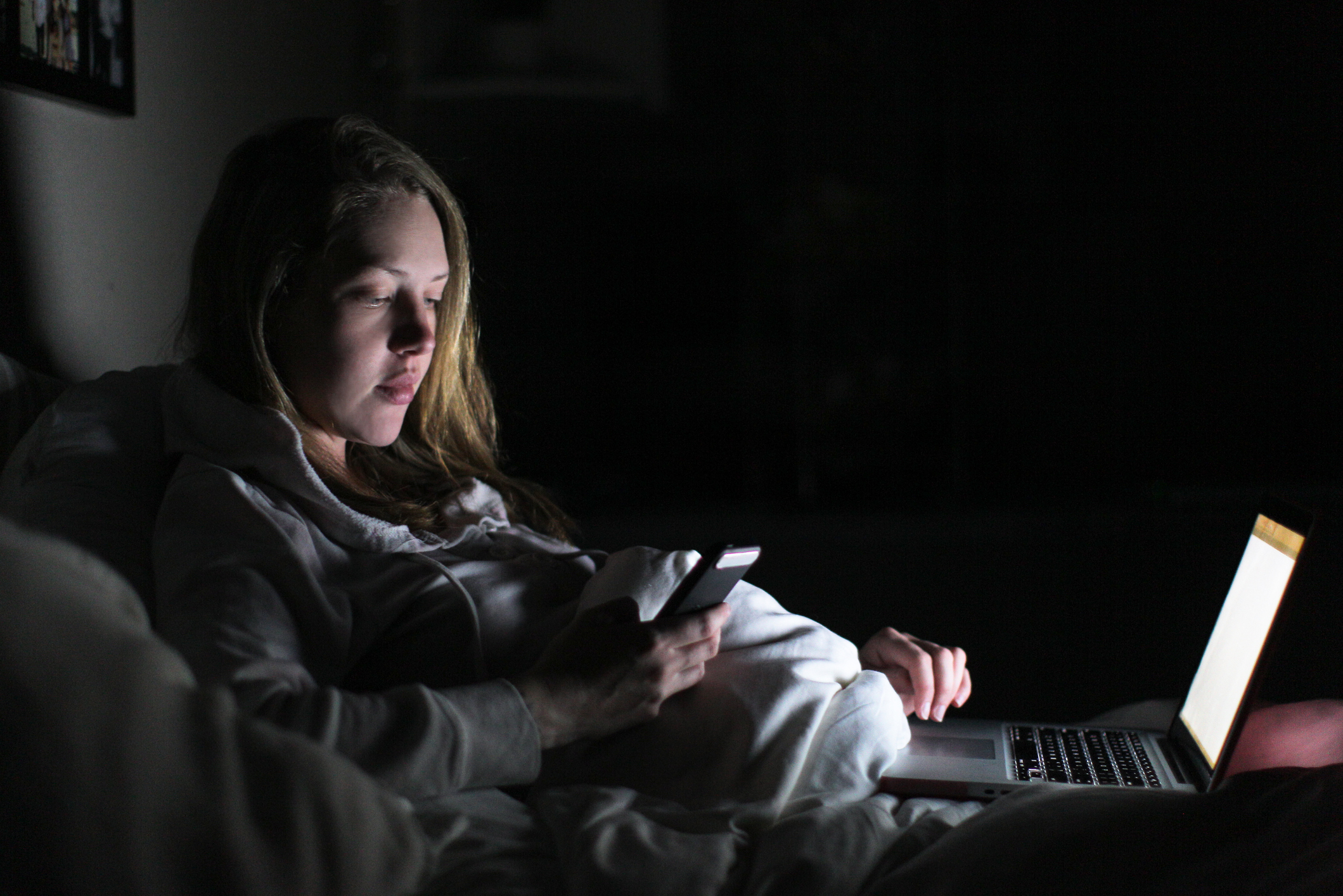 Women on phone and laptop in bed at night