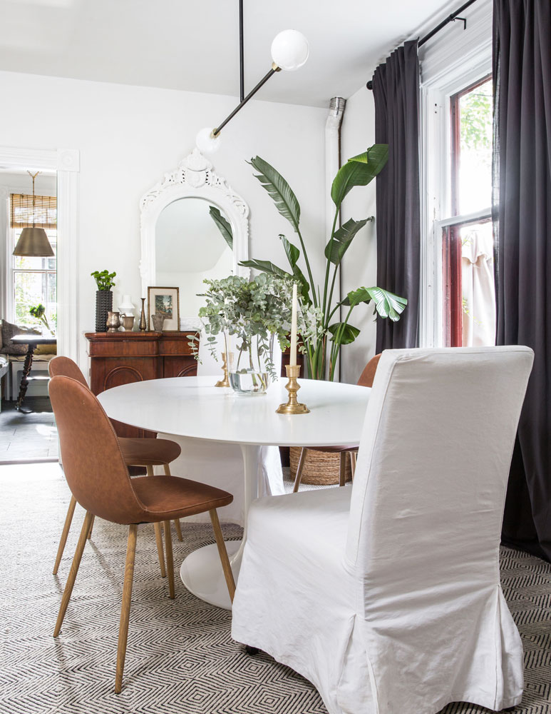 dining area with black curtains, white oval table, mix of chairs, two slip-covered
