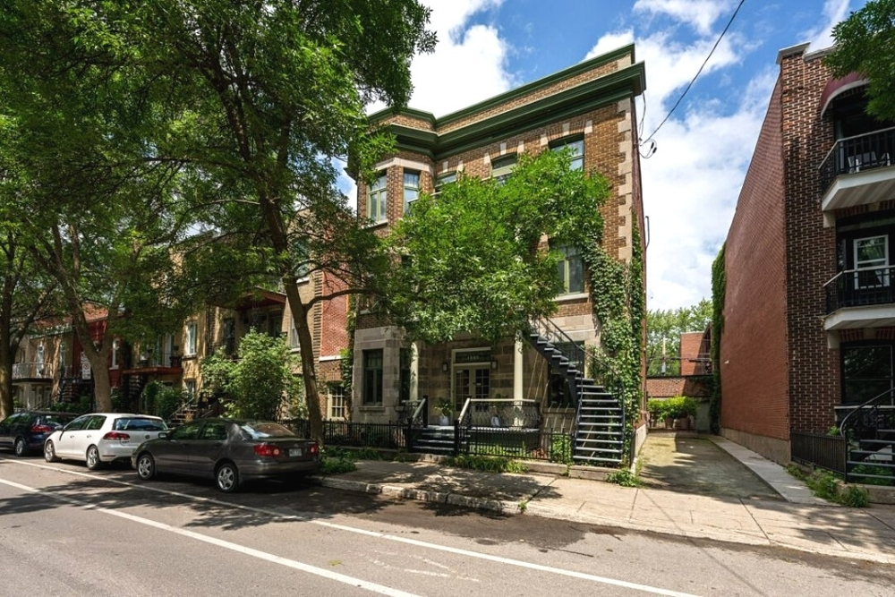 A Victorian-style building in Montreal with staircase and large tree.