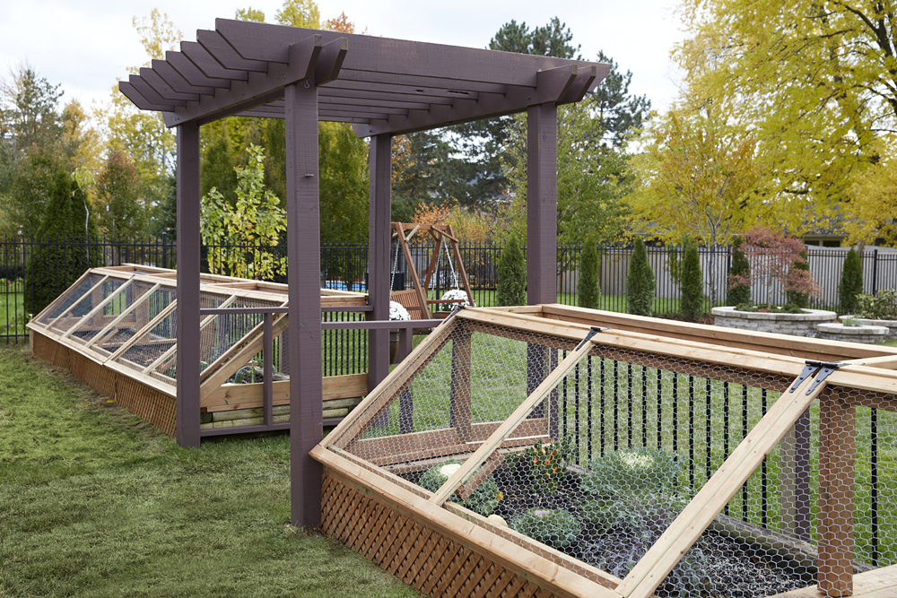 Covered garden area in a spacious backyard with a dark wood pergola separating the two gardening areas