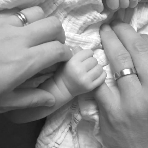 Baby grasping the mom's pinky with dad's hand beside them.