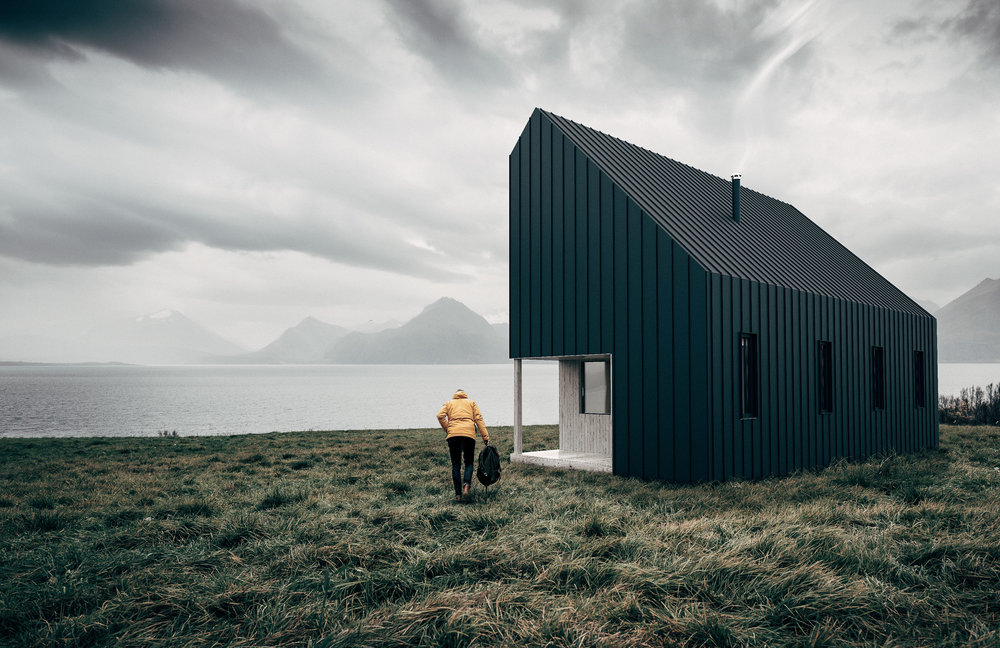 black modular home on grass in front of lake