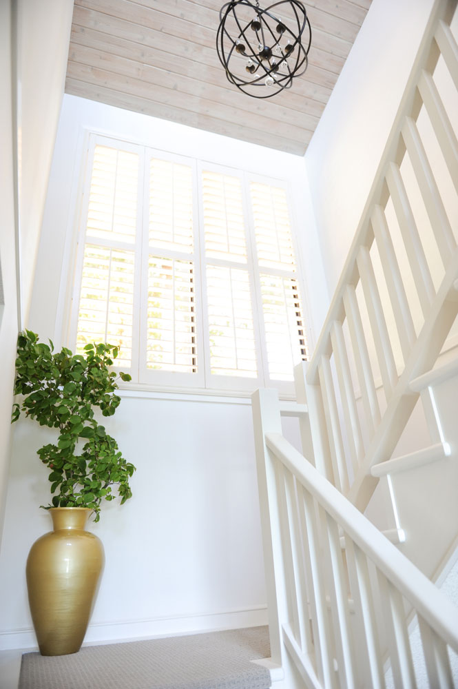 Landing on white staircase with one gold floor vase with greens