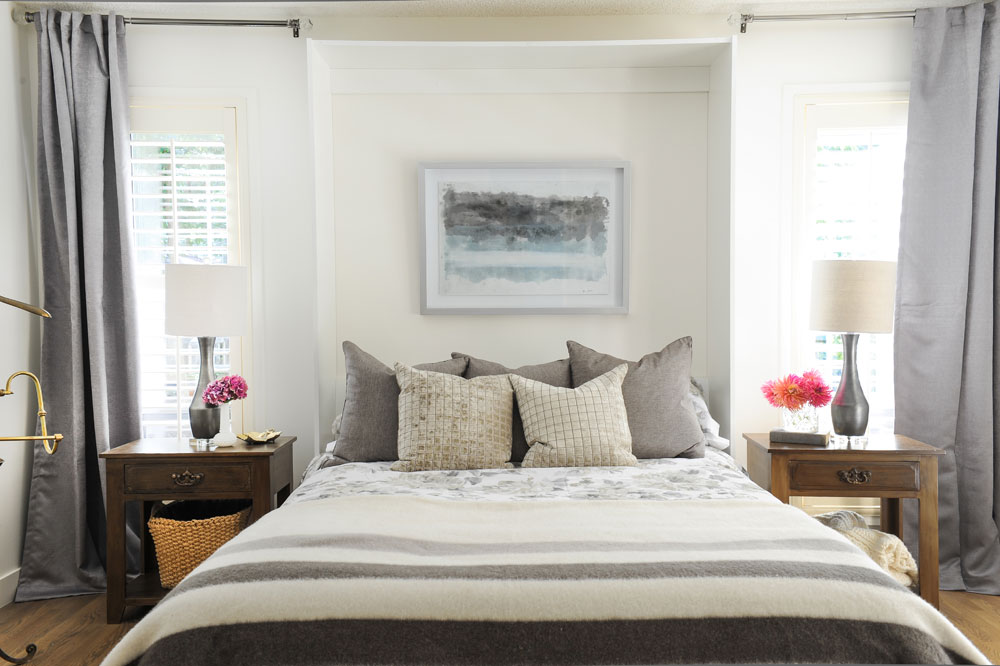 master bedroom with symmetrical tables, lamps, grey curtains and bay blanket on bed