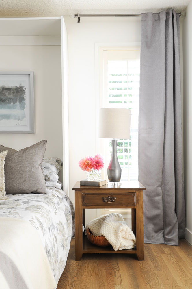 bedside table with blanket beneath and three pink blooms