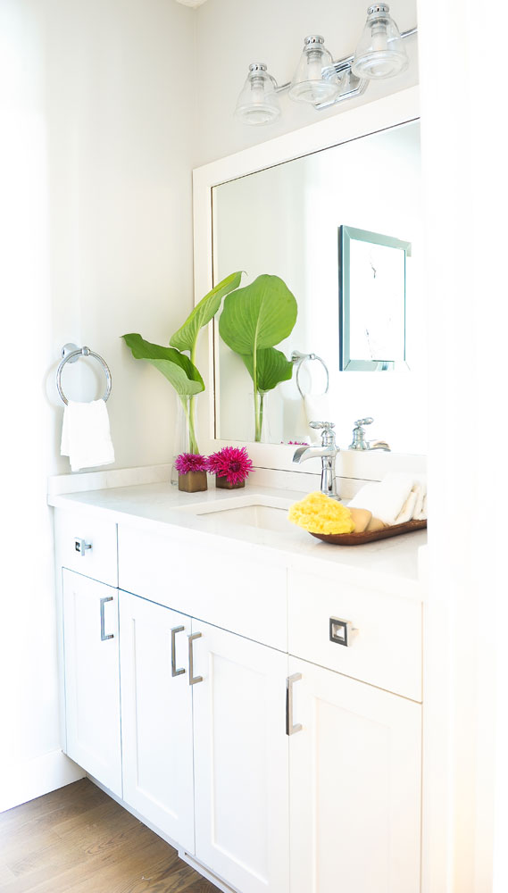 white powder room with square sink, two pink blooms and two palm leaves in corner