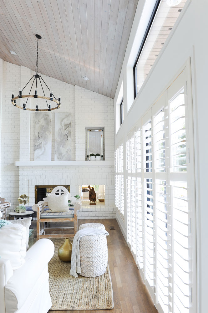 double vaulted white bring living room facing fireplace with shutters along the right side