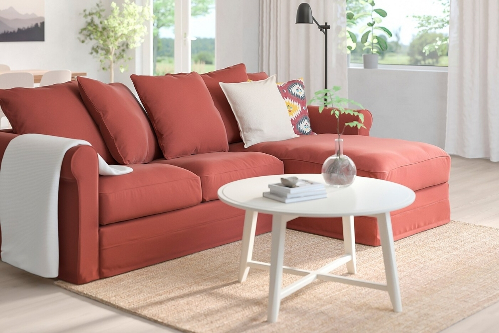 A red three piece sectional on a brown rug and a white circular coffee table.