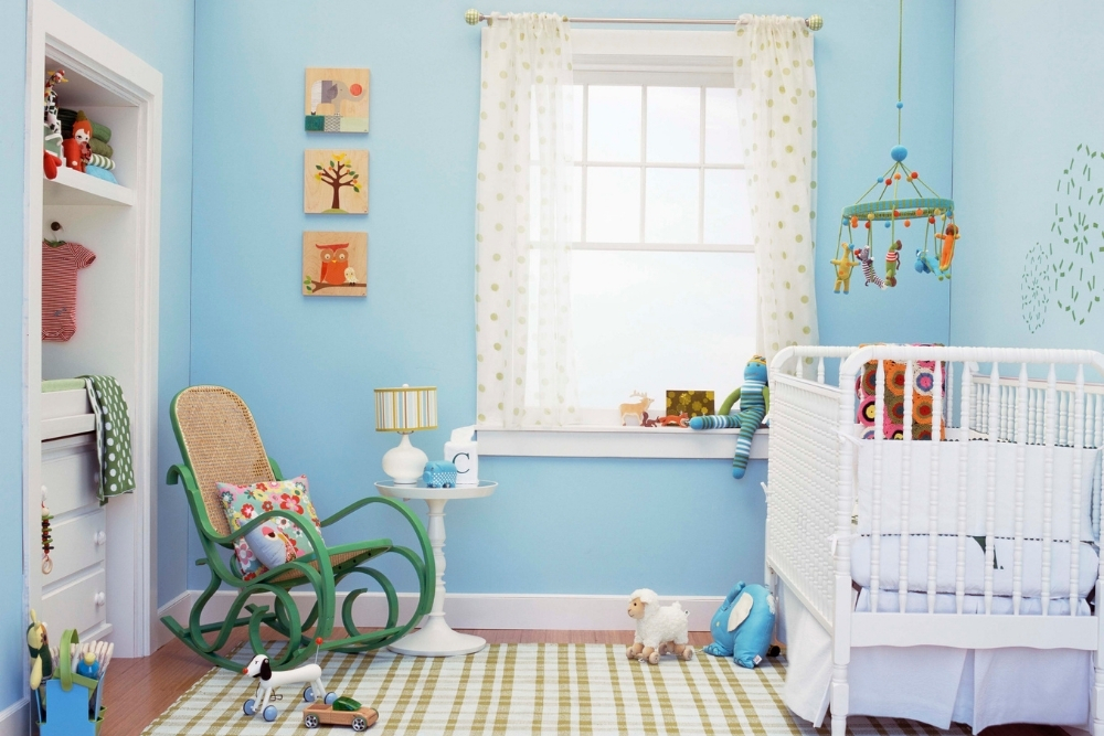 A bright blue baby nursery with a green rug and green rocking chair