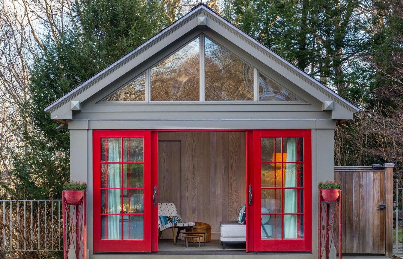 A rustic wood pool cabana with red doors in the backyard