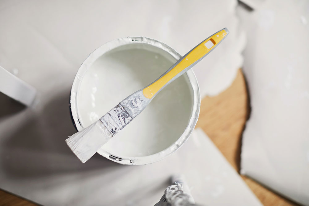 An overhead view of a paint can full of white paint with a paint brush sitting on top