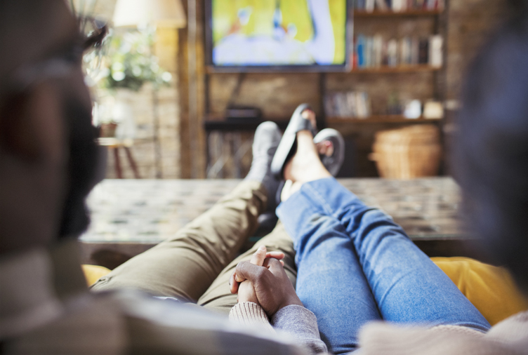 Affectionate couple holding hands, watching TV in living room